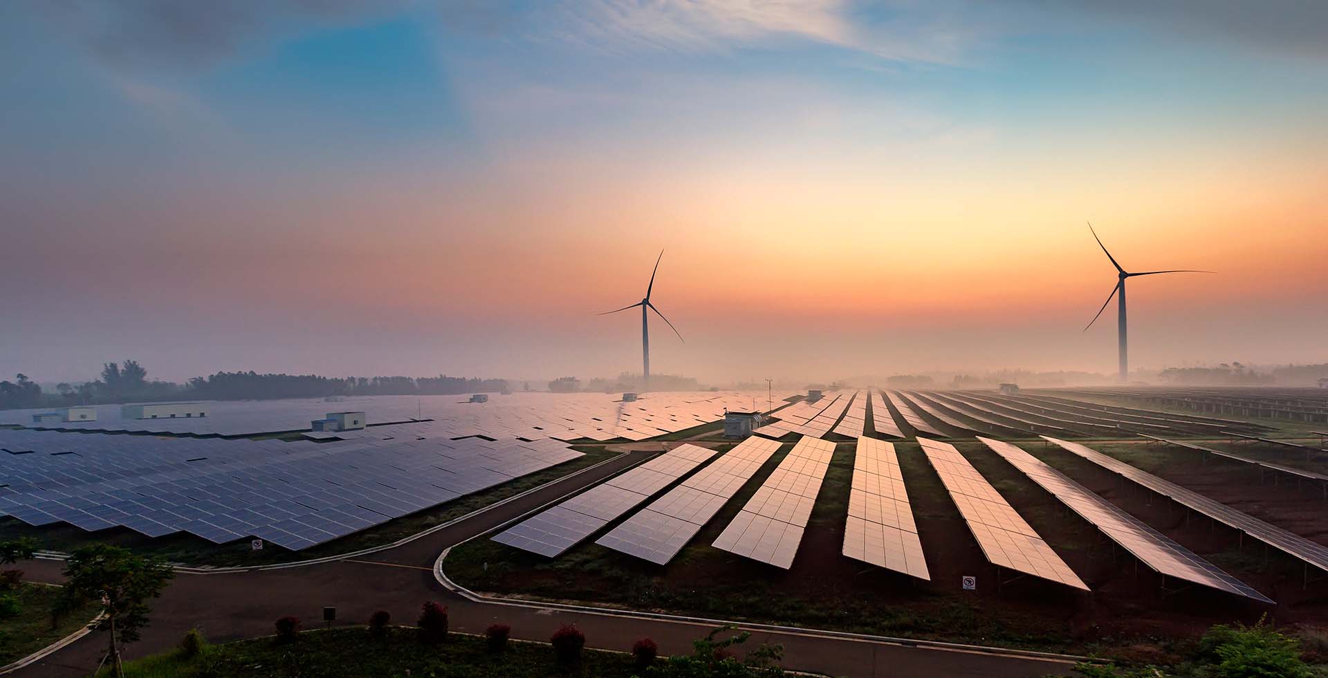 Image of sundown over a solar farm with two wind turbines in the background